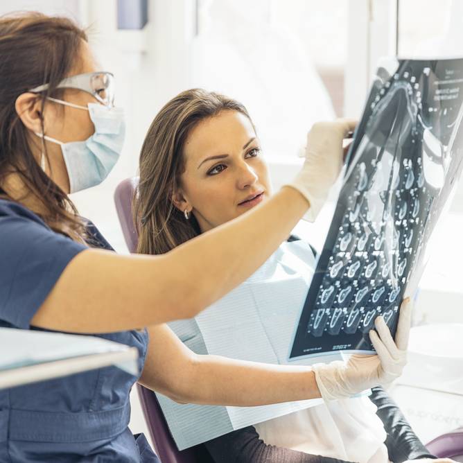 Doctor Talking With Her Patient And Teaching A Radiograph. Dentist